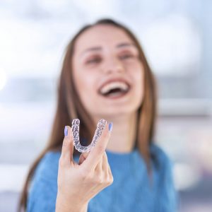 Woman holding Invisalign aligner, representing FAQs about Invisalign at Derby Dental Care.